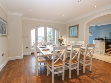 A dining room with a wooden table and white chairs set with plates and glasses at The Little House in Horning