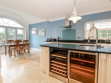 A kitchen with a black countertop island featuring a wine cooler and a dining table with chairs near large windows at The Little House in Horning