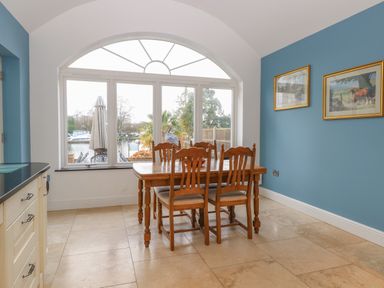 A dining area with a wooden table and chairs next to a large arched window with a view outside at The Little House in Horning