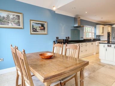 A kitchen with wooden dining table and chairs next to white cabinets and blue walls at The Little House in Horning