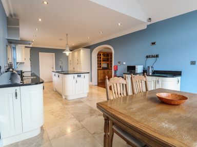 A kitchen with white cabinets blue walls wooden dining table and chairs at The Little House in Horning
