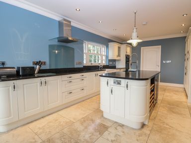 A kitchen with white cabinets black countertops a central island sink and blue walls at The Little House in Horning