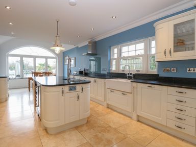 A kitchen with white cabinets black countertops a farmhouse sink a kitchen island and a dining table by a large window at The Little House in Horning