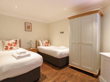A bedroom with two single beds side by side with a nightstand and lamp in between and a wardrobe on the right at The Little House in Horning