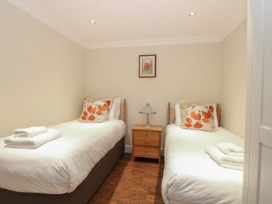 A bedroom with two single beds a wooden nightstand and a lamp at The Little House in Horning
