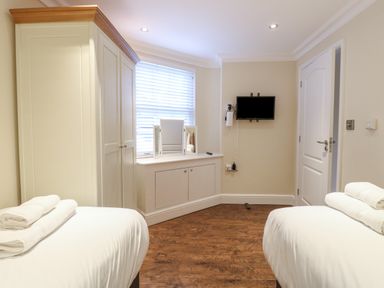 A bedroom with two beds with folded towels on them a wardrobe a wall mounted tv and a window with blinds at The Little House in Horning