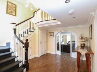 An entryway with a staircase carpeted in gray a wooden table with a model ship and a doorway leading to a living room at The Little House in Horning