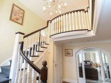 A staircase with white and dark wood railing leading to an upper floor with a modern light fixture above and a living room visible through glass doors at The Little House in Horning