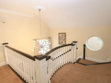 A staircase landing with a curved railing a hanging light fixture a framed picture and a small round window at The Little House in Horning