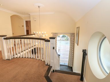 A landing area with white wooden balustrades a hanging light fixture a large arched window with curtains and a round window at The Little House in Horning