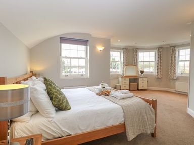 A bedroom with a wooden bed a dressing table with a mirror and windows with curtains at The Little House in Horning