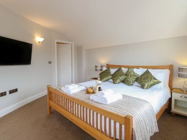 A bedroom with a wooden bed frame white bedding green decorative pillows two bedside tables with lamps and a wall-mounted TV at The Little House in Horning