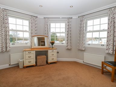 A corner room with three windows floral curtains a dressing table with a mirror and stool and a wooden chair at The Little House in Horning