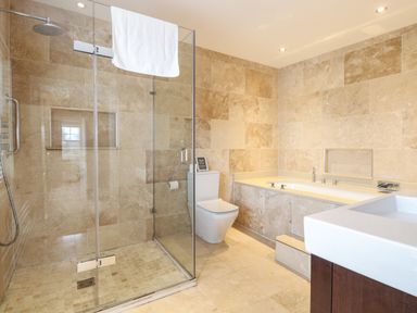 A bathroom with a glass shower enclosure a toilet a bathtub and a sink at The Little House in Horning