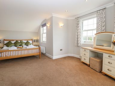 A bedroom with a wooden bed with green pillows and a dressing table with a mirror at The Little House in Horning