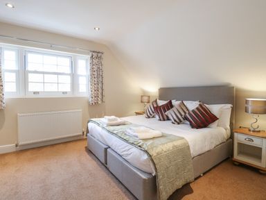 A bedroom with a bed with four pillows bedside tables with lamps and a window with curtains at The Little House in Horning