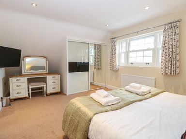 A bedroom with a bed with folded towels a dressing table a stool a wall-mounted TV and a wardrobe with sliding doors at The Little House in Horning