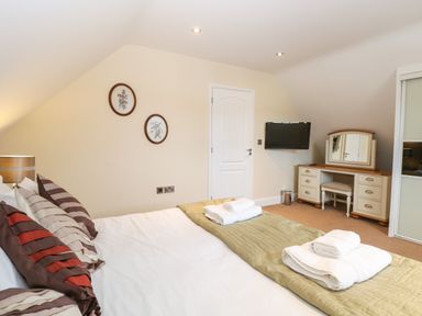 A bedroom with a bed with folded towels on a green blanket a white door a wall-mounted TV and a dressing table at The Little House in Horning