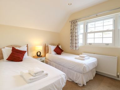A bedroom with two single beds and a window with floral curtains at The Little House in Horning