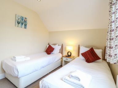 A bedroom with two single beds red cushions white towels on beds and a bedside table with lamp at The Little House in Horning