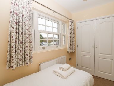 A bedroom with a bed, folded towels, window with floral curtains, radiator and double white closet doors at The Little House in Horning