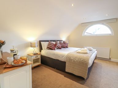 A bedroom with a double bed, pillows, bedside tables with lamps, and a tray with croissants and drinks at The Little House in Horning