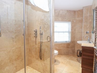A bathroom with a glass shower enclosure a toilet a sink with a wooden cabinet and a window with blinds at The Little House in Horning