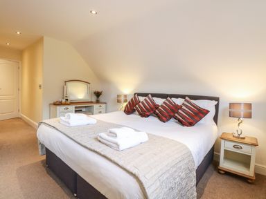A bedroom with a large bed four striped pillows bedside tables lamps and a dressing table at The Little House in Horning