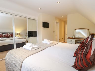 A bedroom with a bed with pillows and towels a dresser with a mirror and a wall-mounted TV at The Little House in Horning