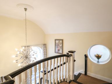 A staircase with white balusters and dark handrail a round window with flowers and a pendant light at The Little House in Horning