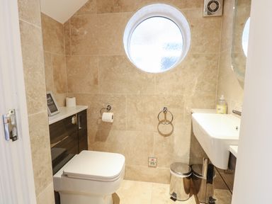 A small bathroom with a toilet, a sink, a circular frosted window, and tiled walls at The Little House in Horning