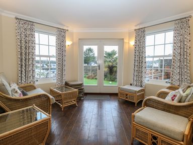 A room with wicker furniture and glass tables with floral curtains on windows and doors at The Little House in Horning