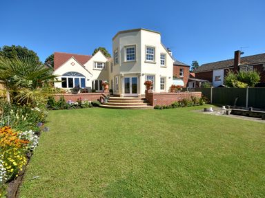 A garden with a lawn and flowers in front of a white house with red roof tiles at The Little House in Horning