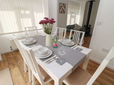 A dining table set with bowls plates cutlery glasses flowers and a bottle in a room with wooden flooring at Butterfly Lodge in Tunstall near Catterick North Yorkshire