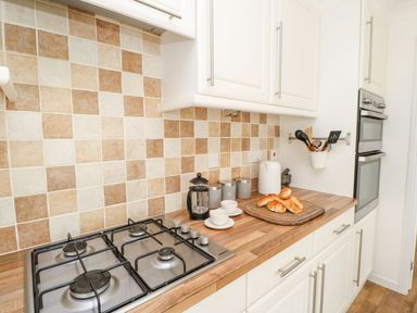 A kitchen countertop with a gas stove, kitchen utensils, canisters, cups, a kettle, croissants on a cutting board and a built-in oven at Butterfly Lodge in Tunstall near Catterick North Yorkshire
