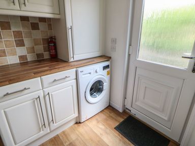 A utility room with a washing machine under a wooden countertop and a white door at Butterfly Lodge in Tunstall near Catterick North Yorkshire