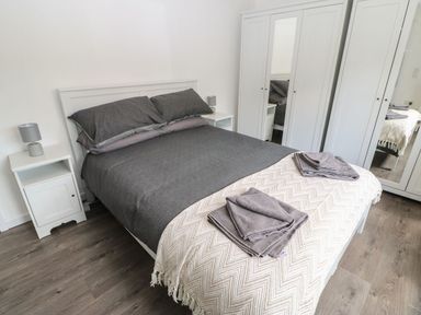 A bedroom with a bed with dark bedding and a cream throw two bedside tables with lamps and a white wardrobe with mirrored doors at Butterfly Lodge in Tunstall near Catterick North Yorkshire