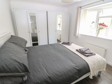 A bedroom with a bed covered in dark grey bedding and folded towels on a cream throw a window with flowers in a vase and white wardrobes with mirrors at Butterfly Lodge in Tunstall near Catterick North Yorkshire