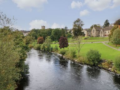 A river flowing through a park with trees and buildings in the background at Butterfly Lodge in Tunstall near Catterick North Yorkshire
