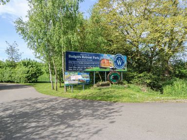 A road entrance with signs for Badgers Retreat Park holiday park surrounded by trees and greenery