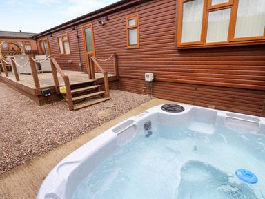 An outdoor hot tub next to a wooden deck and brown wooden building at Butterfly Lodge in Tunstall near Catterick North Yorkshire