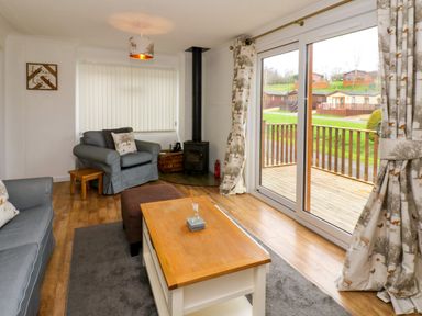 A living room with armchairs coffee table wood stove and sliding doors opening to a deck at Butterfly Lodge in Tunstall near Catterick North Yorkshire