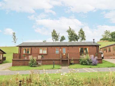 A lodge with a deck and windows at Butterfly Lodge in Tunstall near Catterick, North Yorkshire