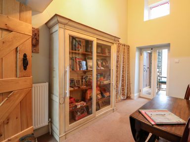 A room with a cabinet filled with books and a table with a chair at Bryn Y Garreg - The Wireless Free Farm (No Tech!) Y Trallwng