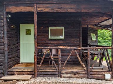 A wooden porch with rustic railing two wooden chairs and a small table at The Log Cabin in Sheldon Blackdown Hills