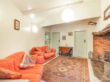 A living room with orange sofas a patterned rug a brick fireplace and wooden doors at The Log Cabin in Sheldon Blackdown Hills