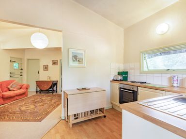A kitchen with a sink stove and a foldable wooden table next to a living room with a red sofa and a wooden drop leaf table at The Log Cabin in Sheldon Blackdown Hills
