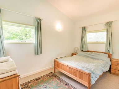 A bedroom with a wooden bed a patterned rug and two small windows with curtains at The Log Cabin in Sheldon Blackdown Hills
