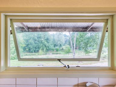 A window partially open showing a green outdoor area with trees at The Log Cabin in Sheldon Blackdown Hills
