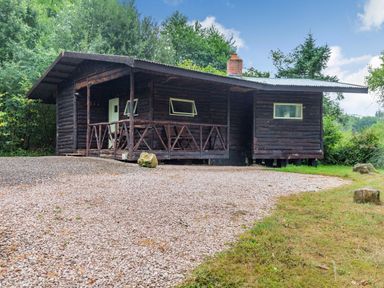 A log cabin with a porch and outdoor furniture surrounded by trees at The Log Cabin in Sheldon Blackdown Hills